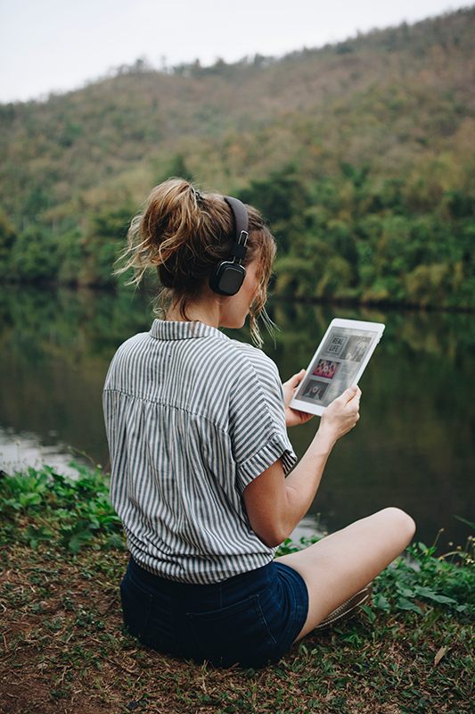 Femme portant des écouteurs assise au bord de la rivière regardant une tablette